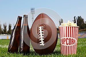 American football ball with beer and popcorn on green field grass in stadium