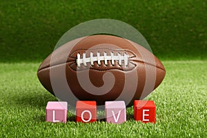 American football ball and cubes with word Love on green grass