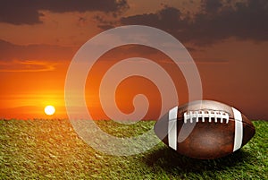 American football ball on green grass field on background of sunset sky. Banner.