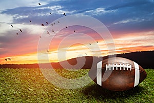 American football ball on green grass field on background of sunset sky. Banner.