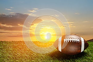 American football ball on green grass field on background of sunset sky. Banner.