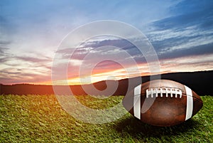 American football ball on green grass field on background of sunset sky. Banner.