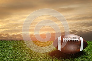 American football ball on green grass field on background of sunset sky. Banner.