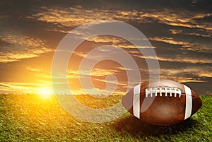 American football ball on green grass field on background of sunset sky. Banner.