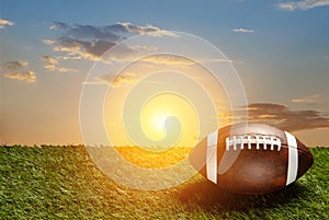 American football ball on green grass field on background of sunset sky. Banner.