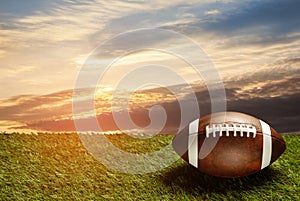 American football ball on green grass field on background of sunset sky. Banner.