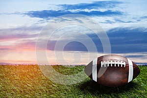 American football ball on green grass field on background of sunset sky. Banner.