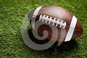 American football ball on green grass field background.