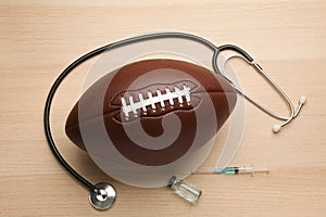 American football ball, stethoscope and drugs on wooden table, flat lay. Doping concept