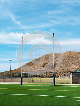 American football goal posts with hill and blue sky.