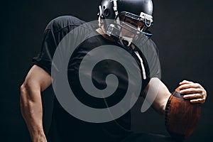 American football player in black sportwear with a ball on black background