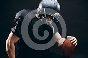 American football player in black sportwear with a ball on black background