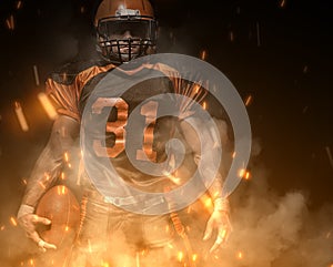 American football player on dark background in smoke and sparks in black and orange outfit