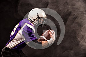American football player holding the ball in his hands. Black background, copy space. The concept of American football