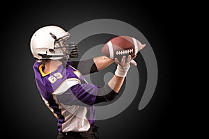 American football player holding ball in his hands in smoke. Black background, copy space. The concept of American