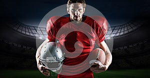 American football player holding rugby ball and helmet against stadium in background