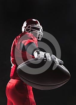 American football player posing with ball on black background