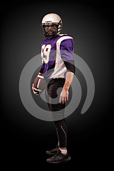 American football player posing with ball on black background