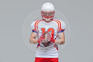 American football sportsman player wearing helmet holding rugby ball isolated on grey background