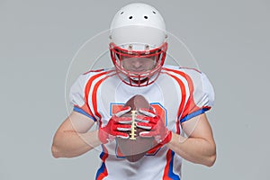 American football sportsman player wearing helmet holding rugby ball isolated on grey background