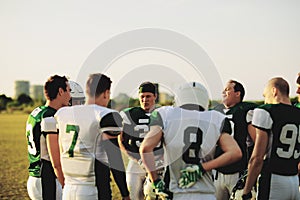 American football team standing in a huddle before practice