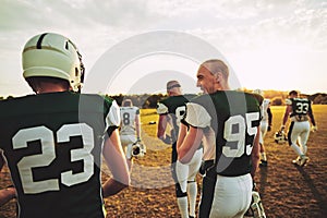 American football teammates walking off a laying field after pra