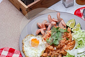 American fried rice served with sausages, cucumbers, shredded vegetables in a gray plate on a white table with seasoning