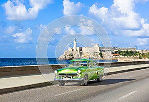 American green 1952 vintage car on the promenade Malecon and in the background the Castillo de los Tres Reyes