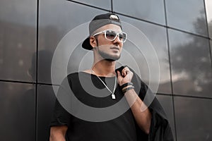 American hipster young man with a beard in a trendy black baseball cap in a stylish t-shirt in white vintage sunglasses