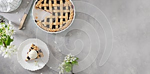 American homemade cherry pie on gray concrete background with flowering branches. Bakery banner. Horizontal, top view, copy space
