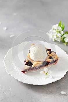 American homemade cherry pie with ice cream on gray concrete background with flowering branches. Vertical, side view, copy space.