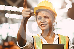 American lady worker in factory maintenance engineer happy working wearing safety uniform and helmet hand pointing and smiling for