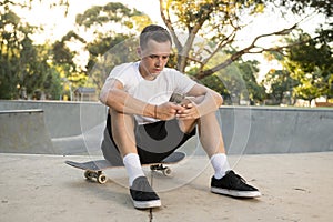 American man 30s sitting on skate board after sport boarding training session using mobile phone sending internet social media tex