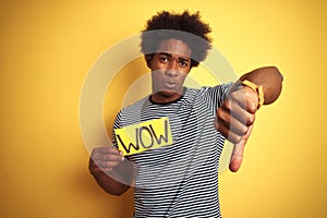 American man with afro hair holding wow banner standing over isolated yellow background with angry face, negative sign showing