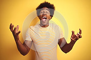 American man with afro hair wearing striped t-shirt standing over isolated yellow background celebrating mad and crazy for success