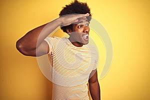American man with afro hair wearing striped t-shirt standing over  yellow background very happy and smiling looking far