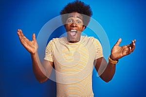 American man with afro hair wearing striped yellow t-shirt over isolated blue background celebrating crazy and amazed for success