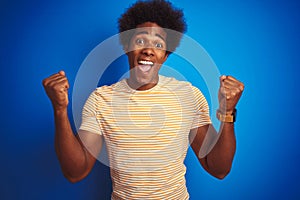 American man with afro hair wearing striped yellow t-shirt over isolated blue background celebrating surprised and amazed for