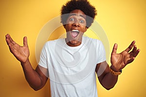 American man with afro hair wearing white t-shirt standing over isolated yellow background celebrating crazy and amazed for