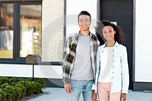 American man and woman standing near new house and looking at camera