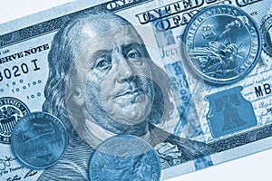 American money: a note of 100 US dollars, coin of 1 dollar, a quarter 25 cents and a penny 1 cent. Blue tinted backdrop or