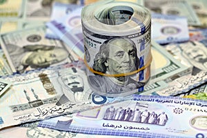 American money roll with a band on a pile of American dollar bills American cash money banknotes with Saudi Arabia riyals money