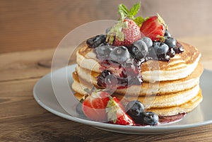 American pancakes or fritters served with strawberry and blueberry jam, delicious dessert for breakfast, rustic style, wooden back