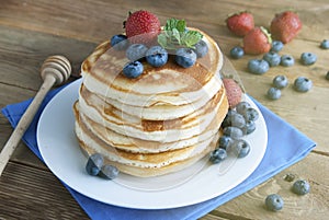 American pancakes or fritters served with strawberry and blueberry jam, delicious dessert for breakfast, rustic style, wooden back