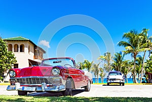 American red convertible 1956 and a blue white 1956 vintage car parked direct on the beach in