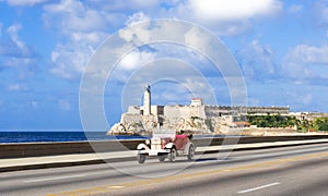 American rose convertible vintage car on the Malecon and in the background the Castillo de los Tres Reyes del Morro in Havana City