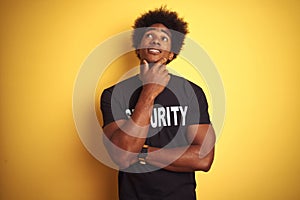 American safeguard man with afro hair wearing security uniform over isolated yellow background with hand on chin thinking about