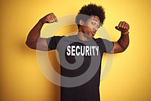 American safeguard man with afro hair wearing security uniform over isolated yellow background showing arms muscles smiling proud