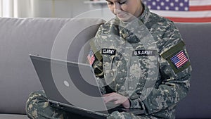 American servicewoman typing laptop and smiling on camera, searching information