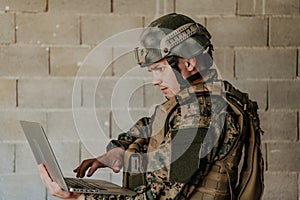 American soldier in military uniform using laptop computer for drone controlling and to stay in contact with friends and